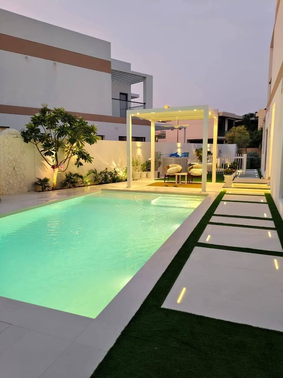 Backyard pool landscaping with pergola seating and garden lights in Abu Dhabi